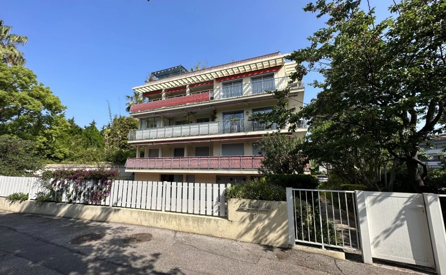 Apartment building with a gated entrance with blue skies and trees surrounding it